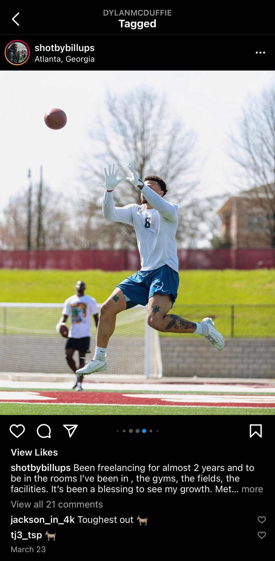 Football player in white jersey and blue shorts catching a ball outdoors on a field.