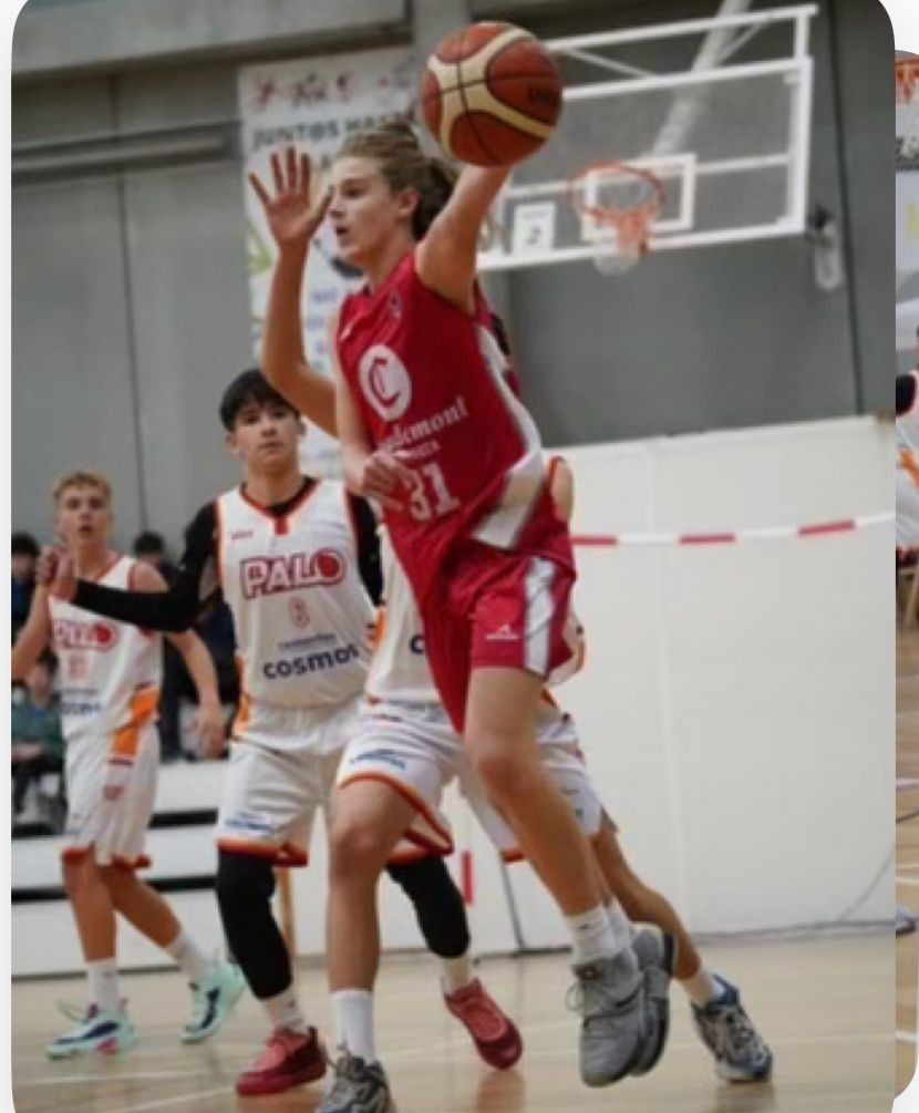 Basketball player in red jersey jumping to make a shot with defenders nearby on an indoor court.